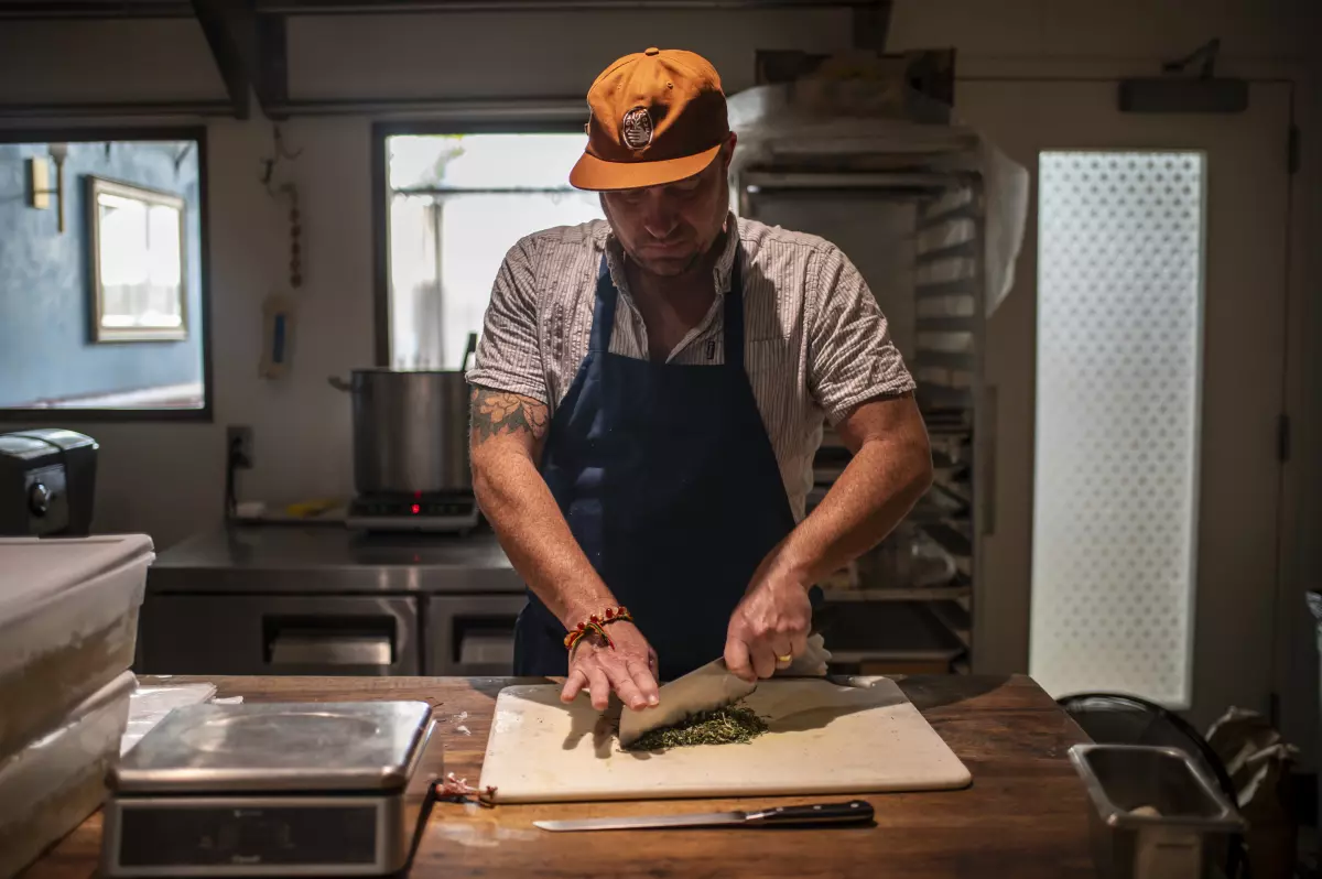 Tedesco chops rosemary in the kitchen. He hopes the pay-what-you-will promotion can be a way to meet the current affordability and social challenges facing Americans.