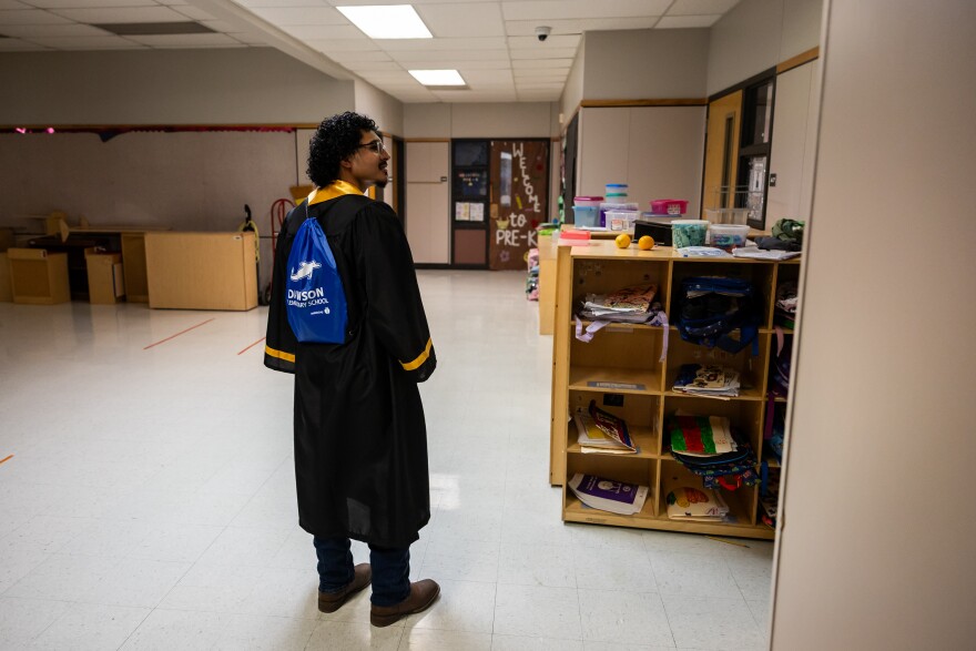 A young man wearing a black gown and a drawstring backpack that reads "Dawson"