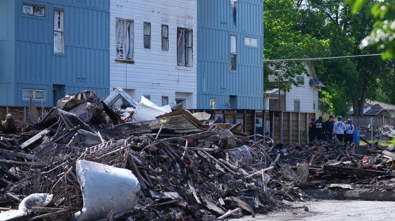 Officials stand near rubble following an apartment complex fire, Friday,...