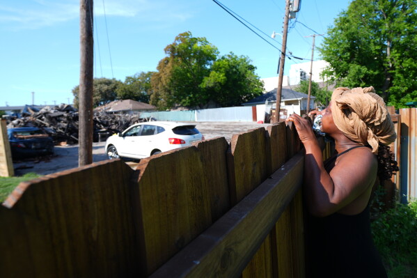 Trish Thompson looks over a fence at the damage left behind following an apartment complex fire not far from where she lives, Friday, May 29, 2026, in Dallas. (AP Photo/Julio Cortez)