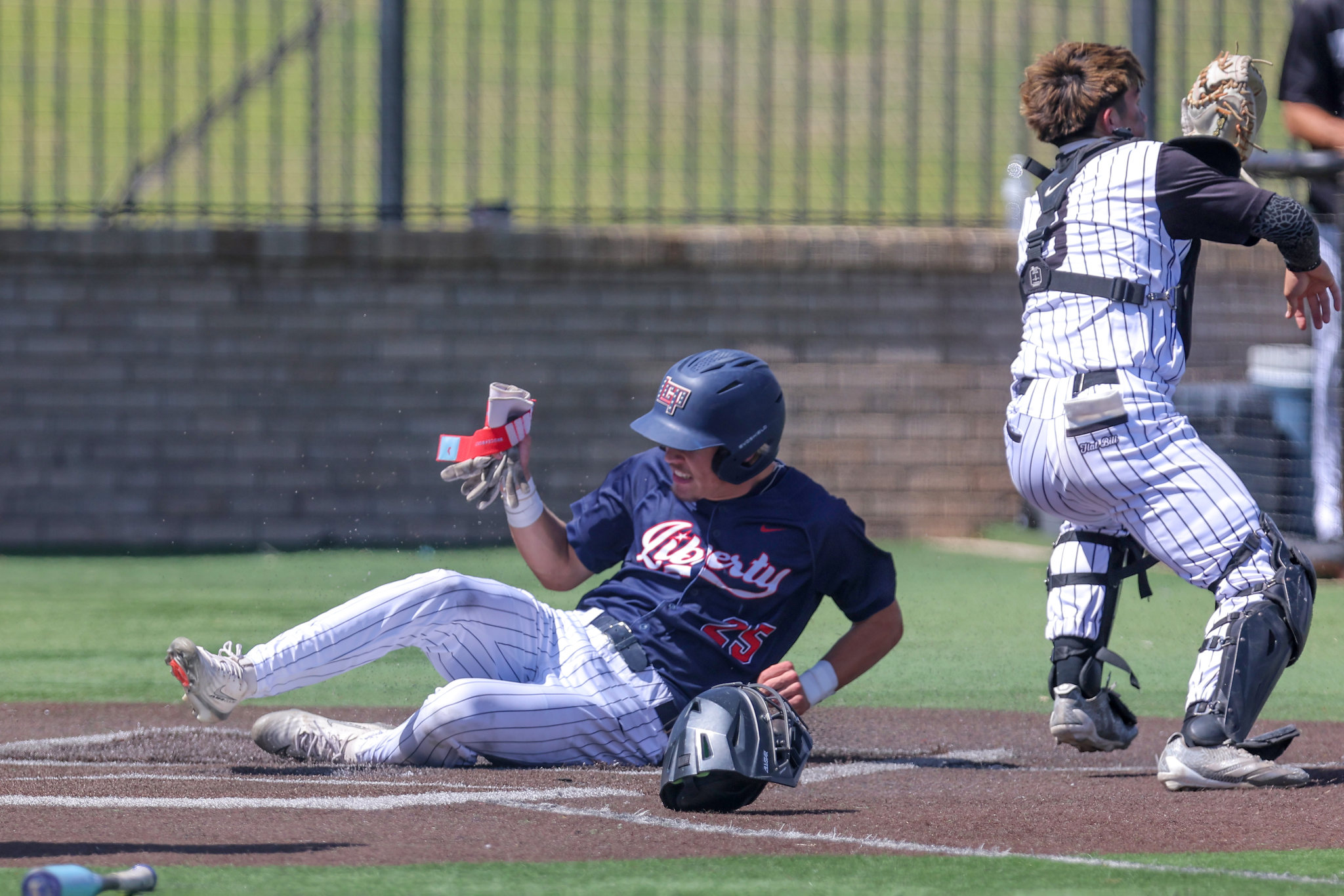 Baseball play at home plate: a sliding baserunner in navy jersey and a catcher in white-pinstripe gear collide near the plate on the dirt infield.