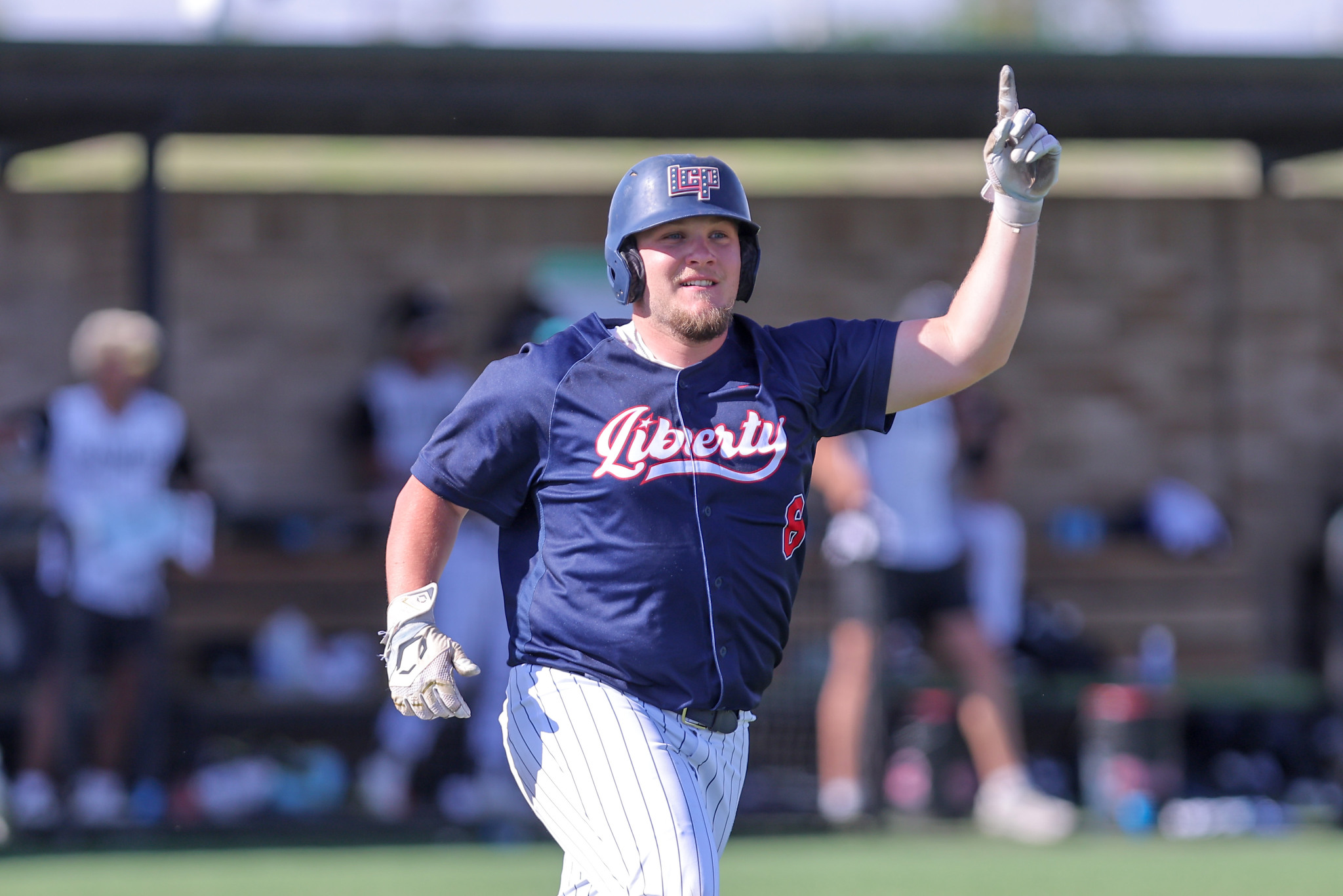 Baseball player in navy Liberty uniform raises right index finger in celebration on the field at a game event.