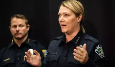 A woman in a police uniform gestures as a man in an EMS uniform looks on behind her