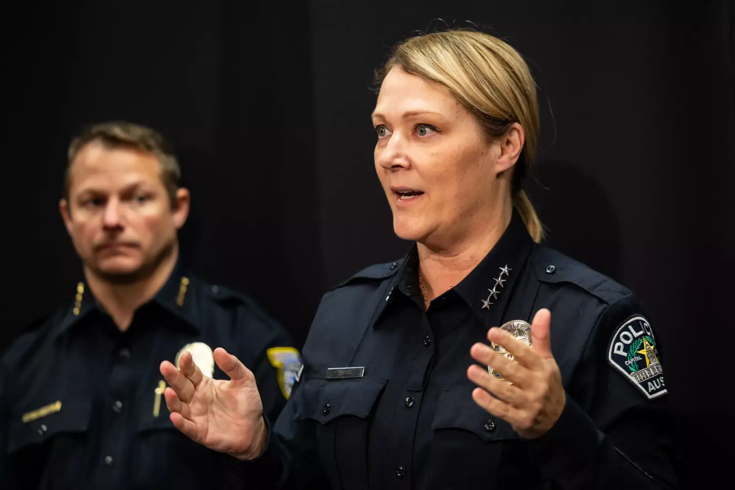 A woman in a police uniform gestures as a man in an EMS uniform looks on behind her
