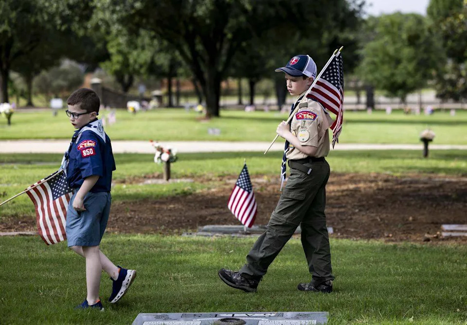 Charles and Leo Devine, 8 and 11 years old, with Scouting America, check graves for symbols indicating military service at Bluebonnet Hills Funeral Home & Memorial Park on Saturday, May 23, 2026 in Colleyville. The scouts were part of a group volunteering to put out flags ahead of a Memorial Day service taking place at the cemetery on Monday.