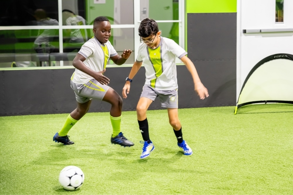 Two kids kicking the soccer ball during class at KidsUnited.