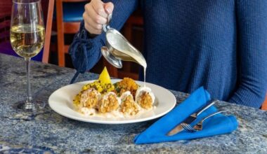 Woman pouring sauce over seafood meal with a glass of white wine.