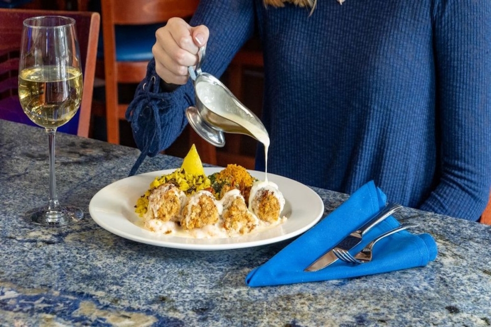 Woman pouring sauce over seafood meal with a glass of white wine.