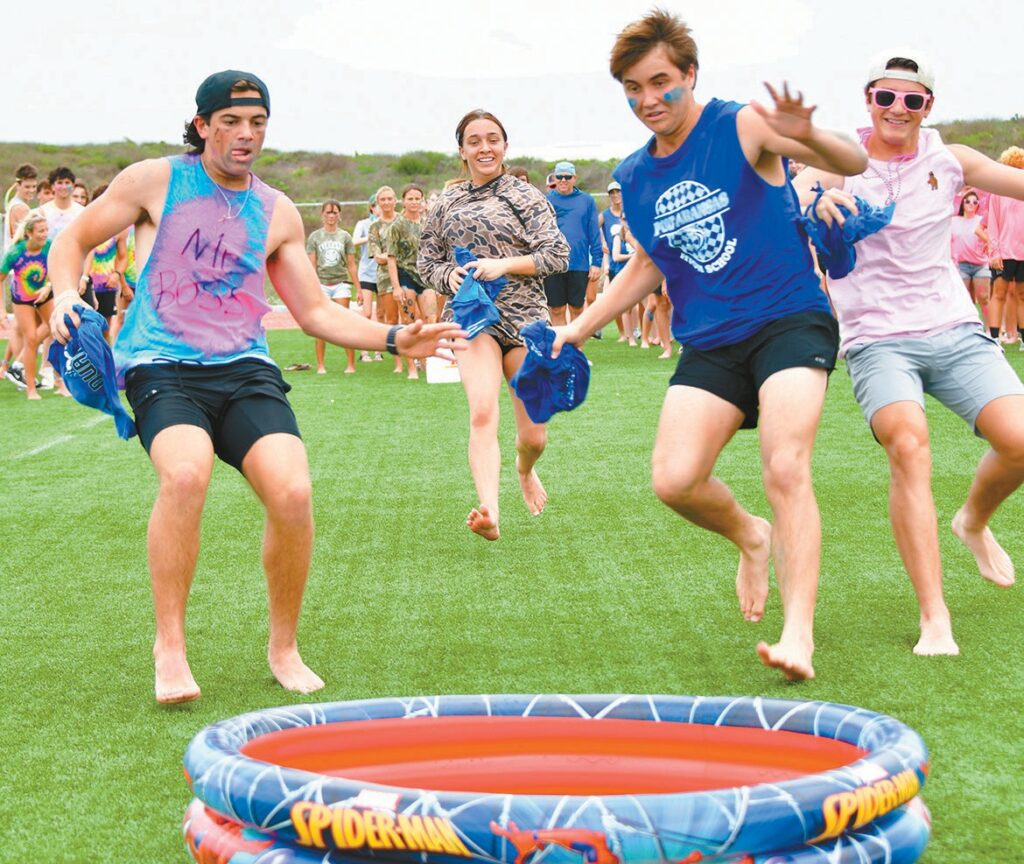 Port Aransas High School students Caden Meyer, senior, Lilly Nixon, junior, Eli Derkits, sophomore, and Julian Meyer, freshman, run to dunk a shirt in water in a relay game where participants had to get a shirt wet and run it back to the next player.