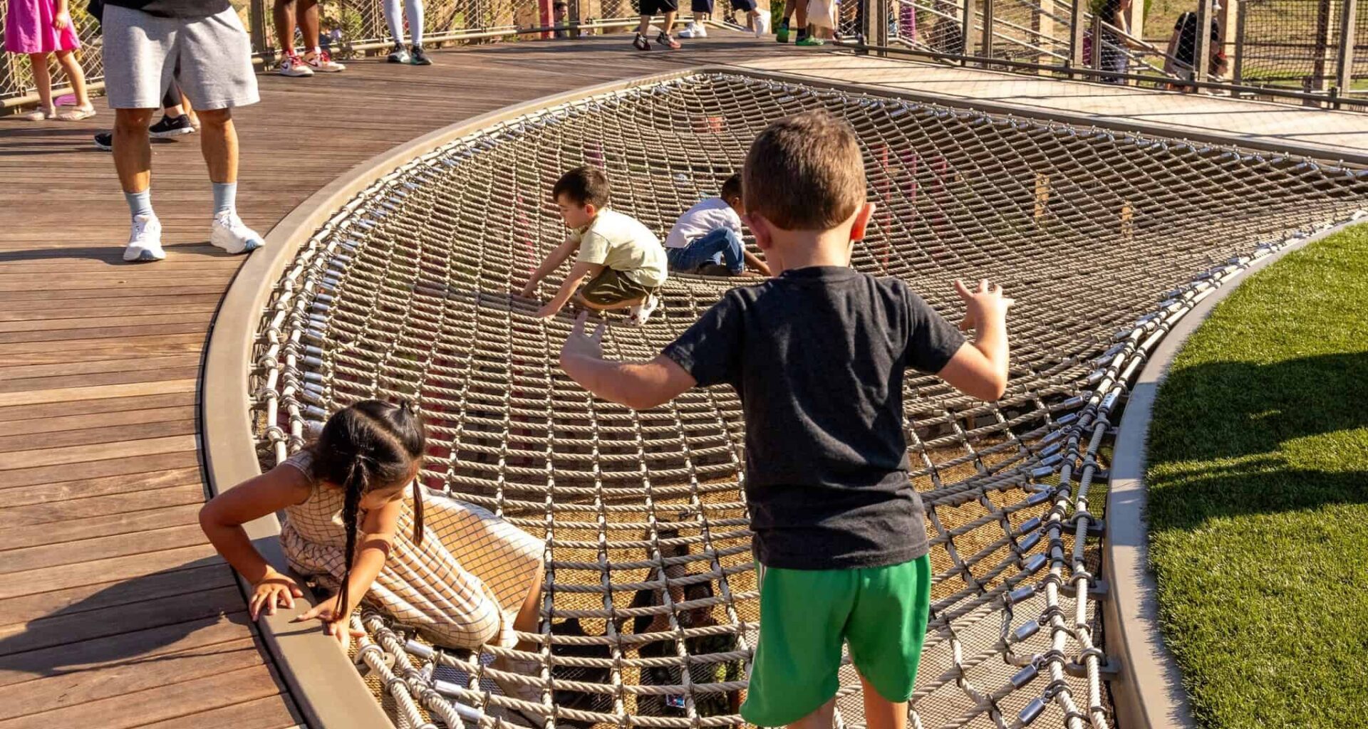 Children climbing on a large net playground structure in a park setting.