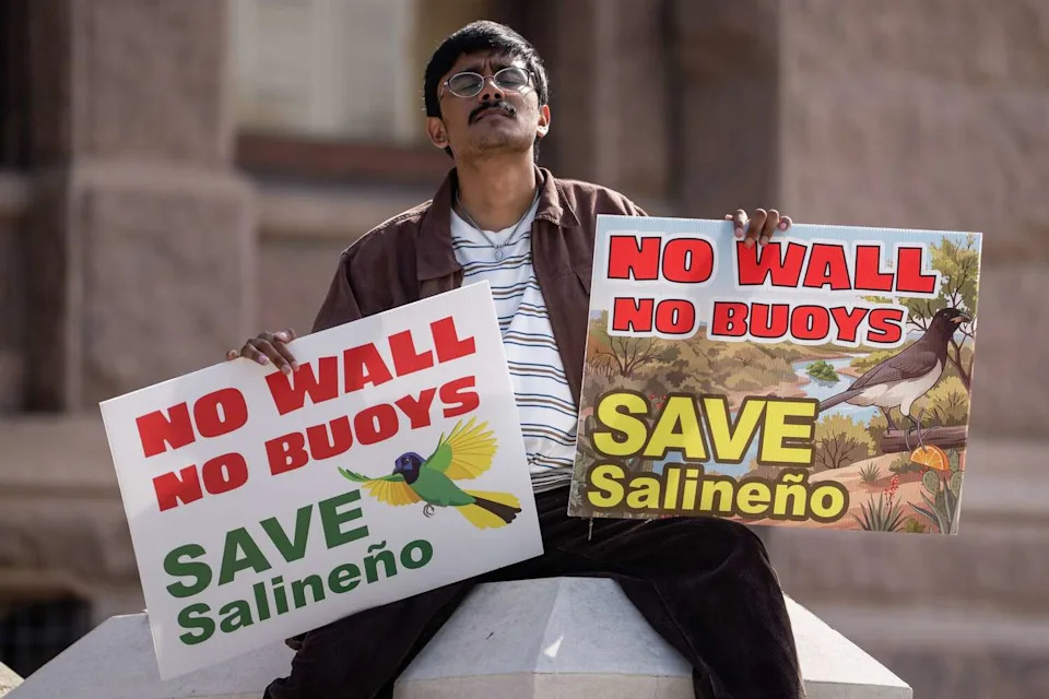 Alexis Esparza holds signs as he listens to speakers at a rally against continued border wall expansion in the Big Bend region, hosted by the Texas Says No Border Wall coalition at the Texas State Capitol, May 19, 2026. (Sara Diggins/Austin American-Statesman)