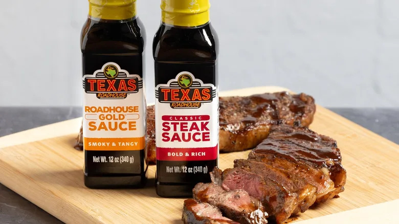 Two bottles of Texas Roadhouse's steak sauces sitting on a cutting board with steaks