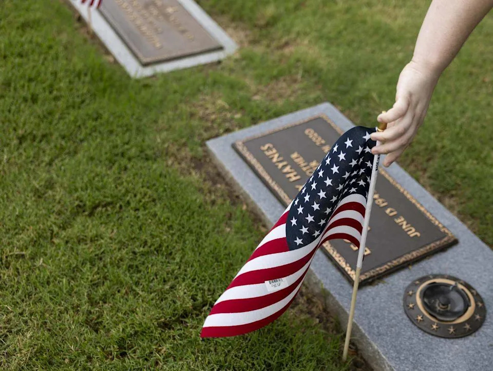 Kara Jakubik, 17, with Scouting America, marks a grave with a U.S. flag at Bluebonnet Hills Funeral Home & Memorial Park ahead of Memorial Day on Saturday, May 23, 2026 in Colleyville.