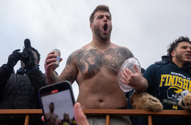 Michigan’s Trevor Keegan holds a beer in one hand and the 2023 National Championship trophy in the other during a parade at the University of Michigan campus in Ann Arbor on Saturday, Jan. 13, 2024.