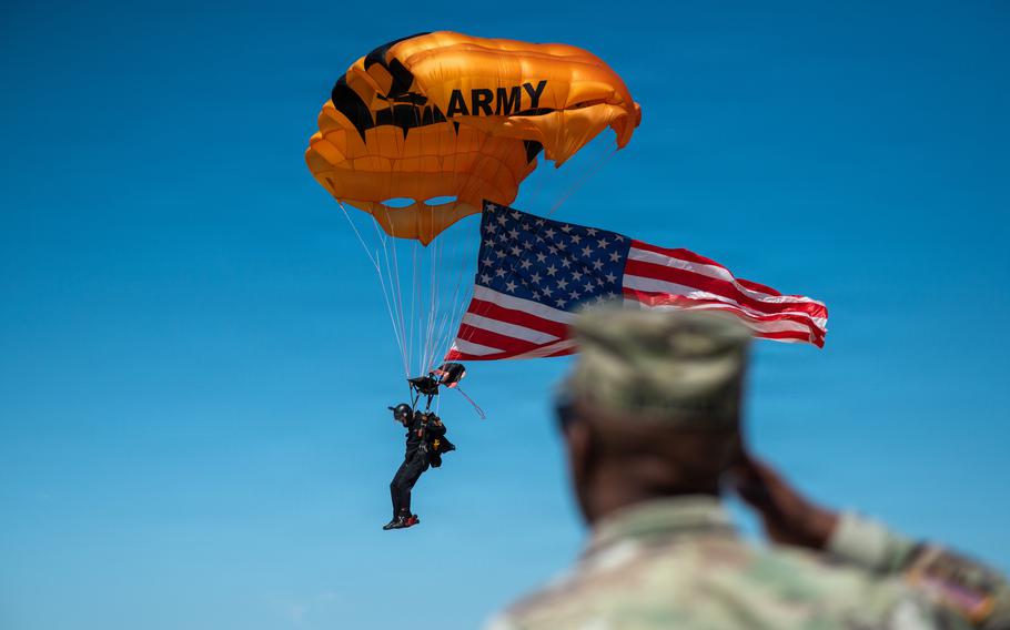 A soldier salutes a parachuter as he descends from the sky with an American flag.