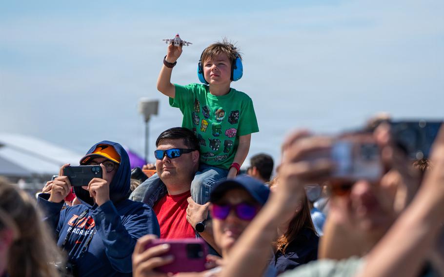 A young boy sits on a man’s shoulders and holds a toy airplane in the air.