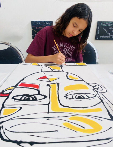 A photograph of a girl painting a large abstract portrait.