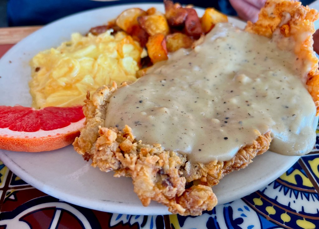 a chicken fried steak with eggs and potatoes