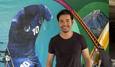 Betirri smiles in front of the Gateway Mural in his studio