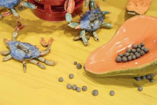 A detail view of ceramic artworks depicting softshelol crabs and fruit on a yellow surface.