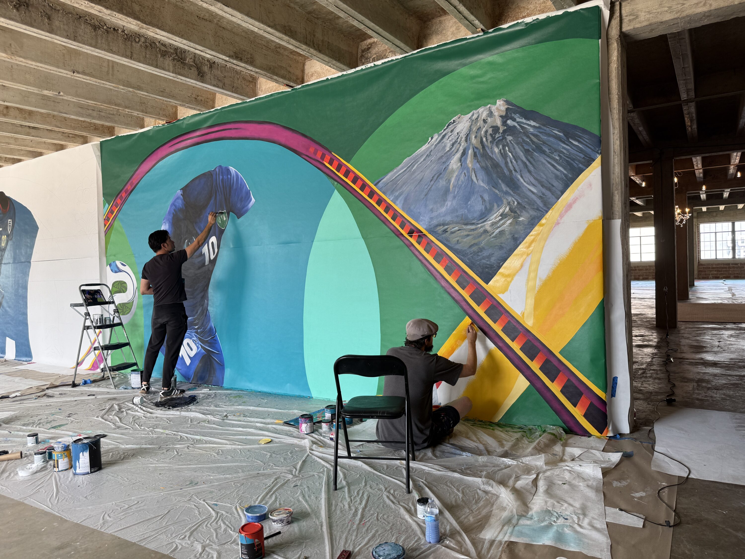 Two artists work on painting a section of a mural