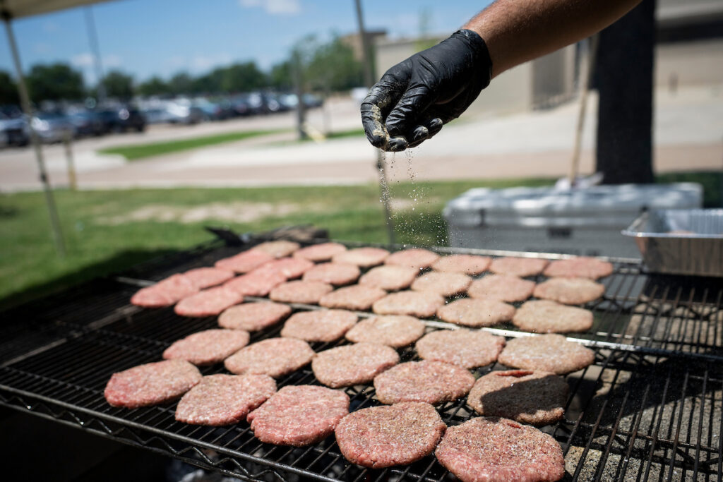 Burgers on a grill being seasoned