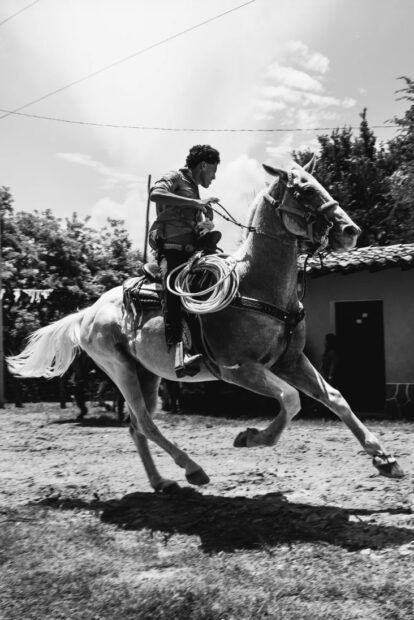 A black and white image of a person riding a horse.