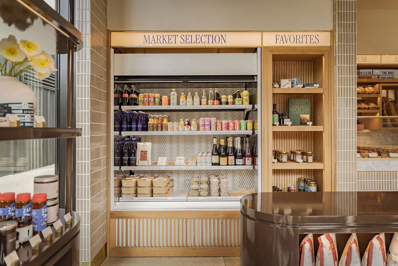 Refrigerated shelves in a store display bottled drinks, packaged foods, and jars. Adjacent open shelves hold more food items under signs reading "Market Selection" and "Favorites.