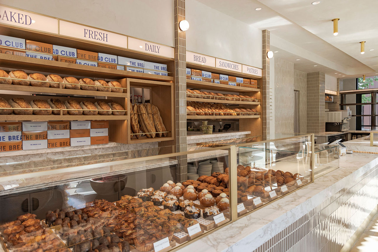 A bakery interior with shelves of assorted bread loaves and baguettes, and glass display cases filled with pastries and baked goods.