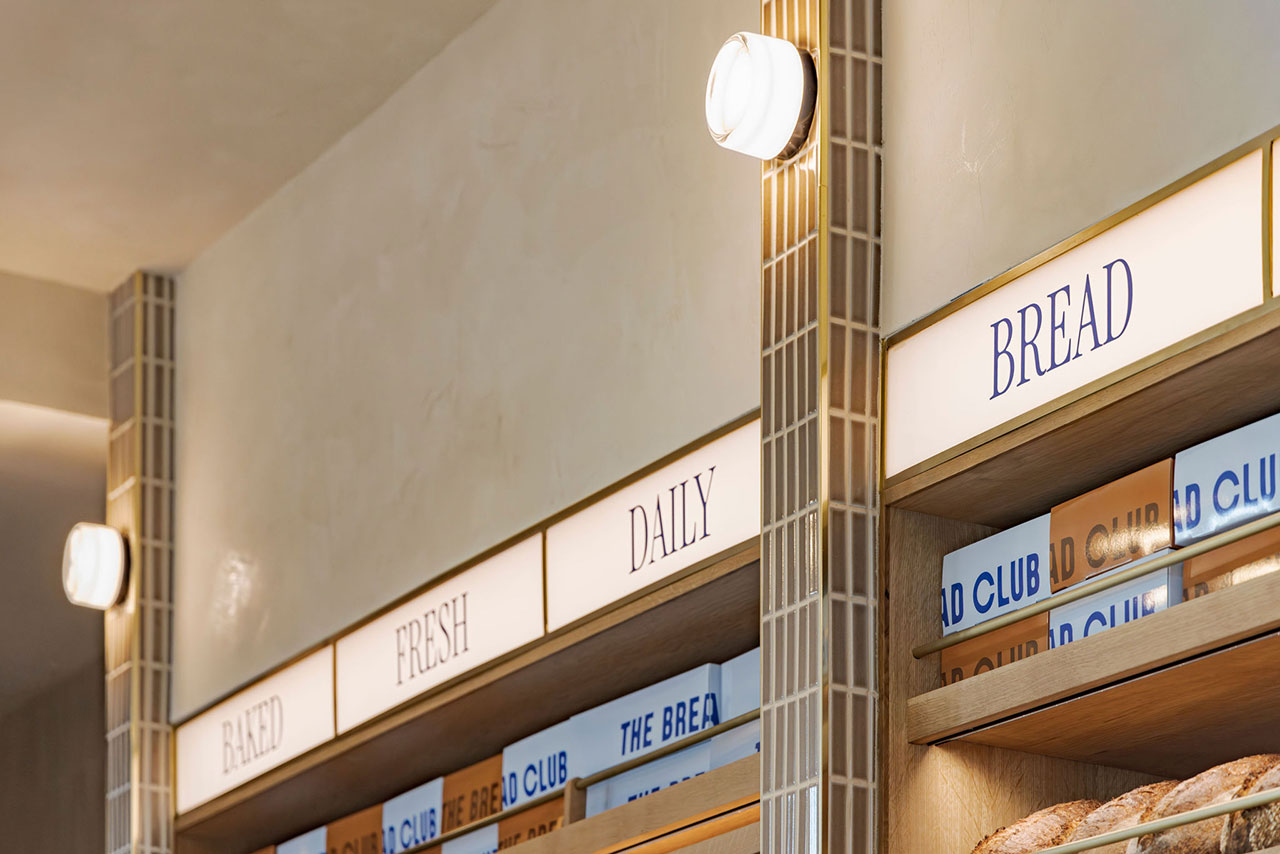 Illuminated bakery signage displays the words "BAKED FRESH DAILY BREAD" above shelves stocked with loaves and packages of bread.