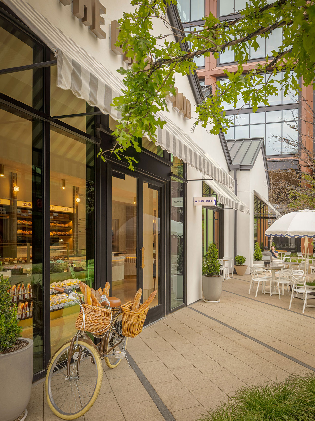 A bakery café with large windows, outdoor seating, and a bicycle with baskets of baguettes parked by the entrance.
