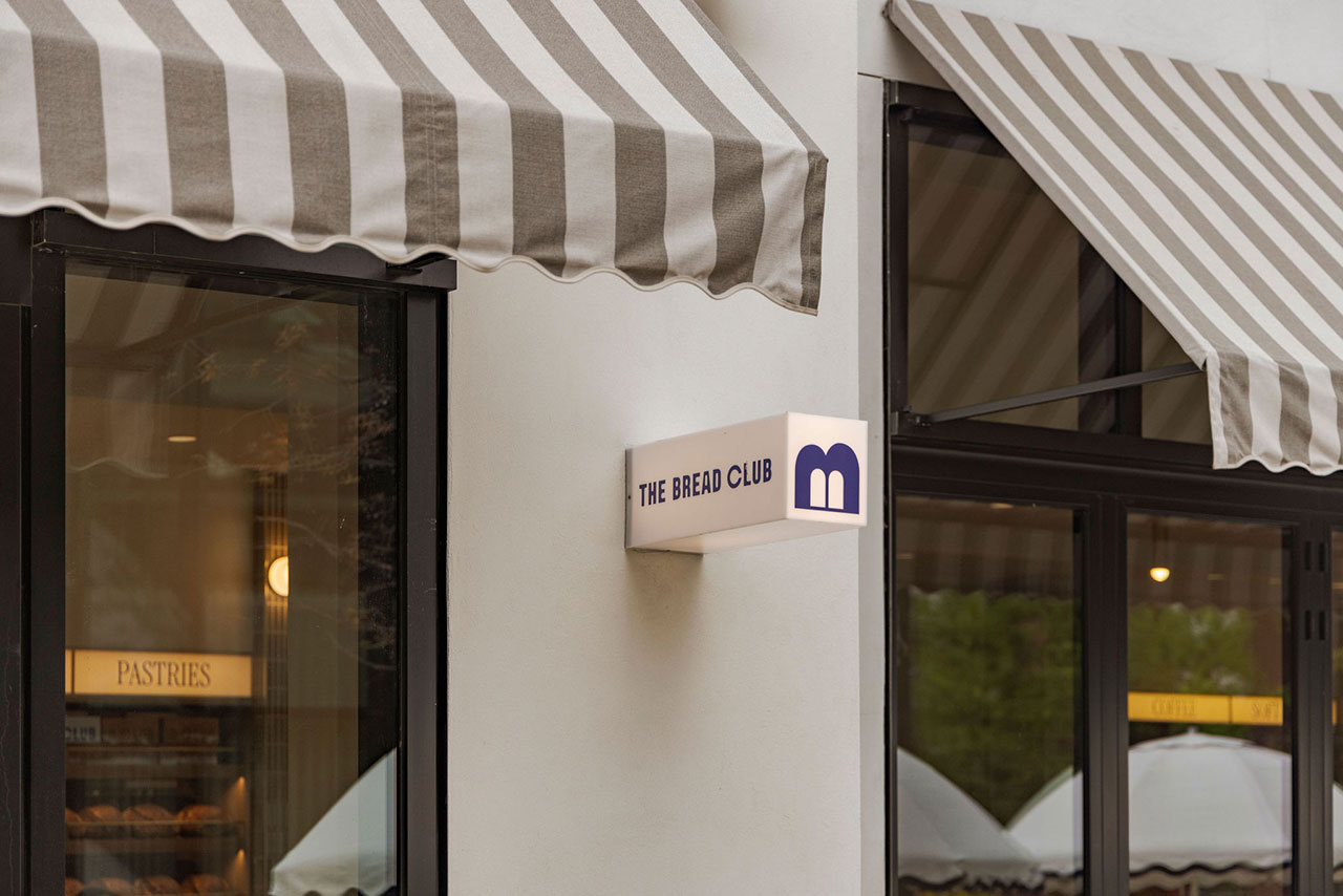 Exterior of a bakery with striped awnings, a sign reading "The Bread Club," and a window displaying the word "Pastries.