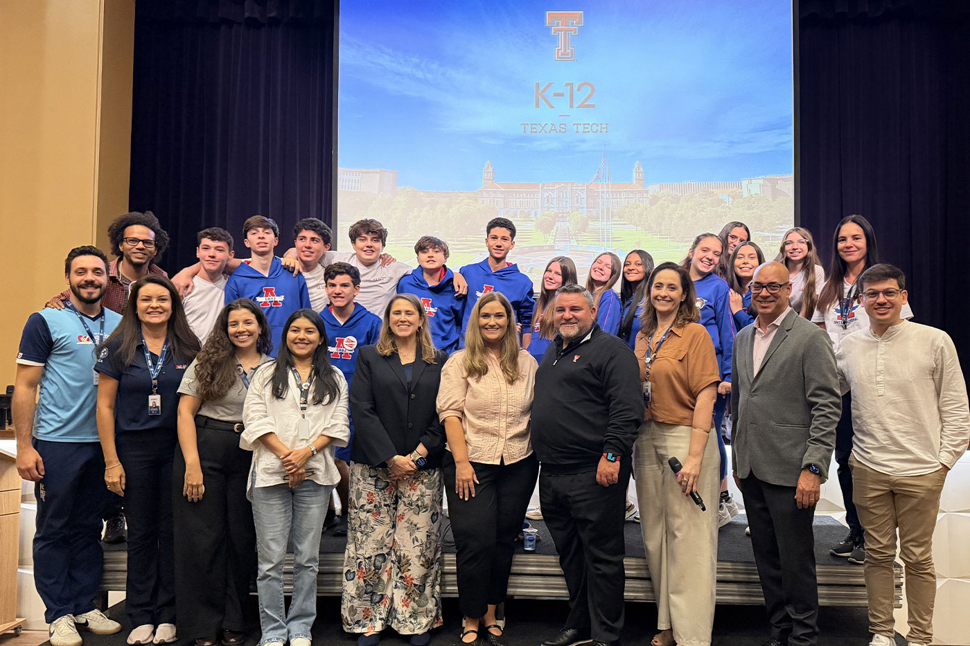A group of 26 administrators, teachers and students pose on stage