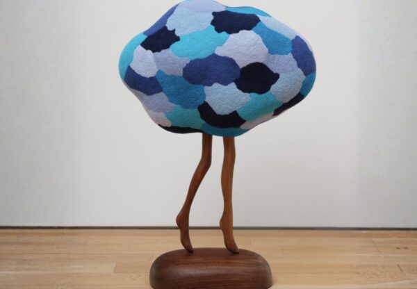 A sculpture of a globular shape atop wooden legs on a wooden base. 