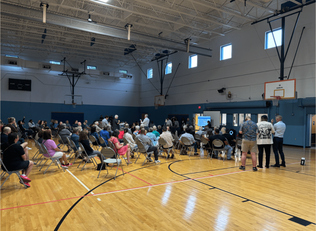 Oak Cliff community meeting in large gym, with the TV in the background.
