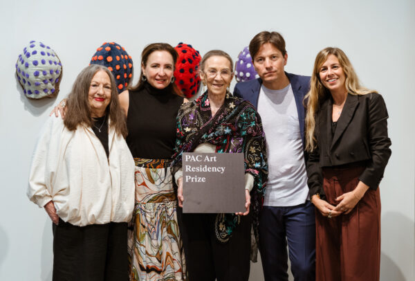 A group portrait of philanthropist Paola Creixell and artist Teresa Serrano, in front of her artwork hanging on a white wall.