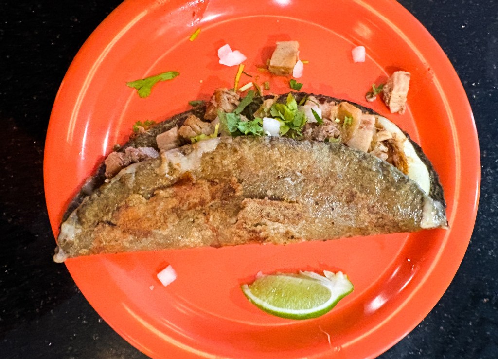 a blue corn tortilla rib eye taco on an orange plate.