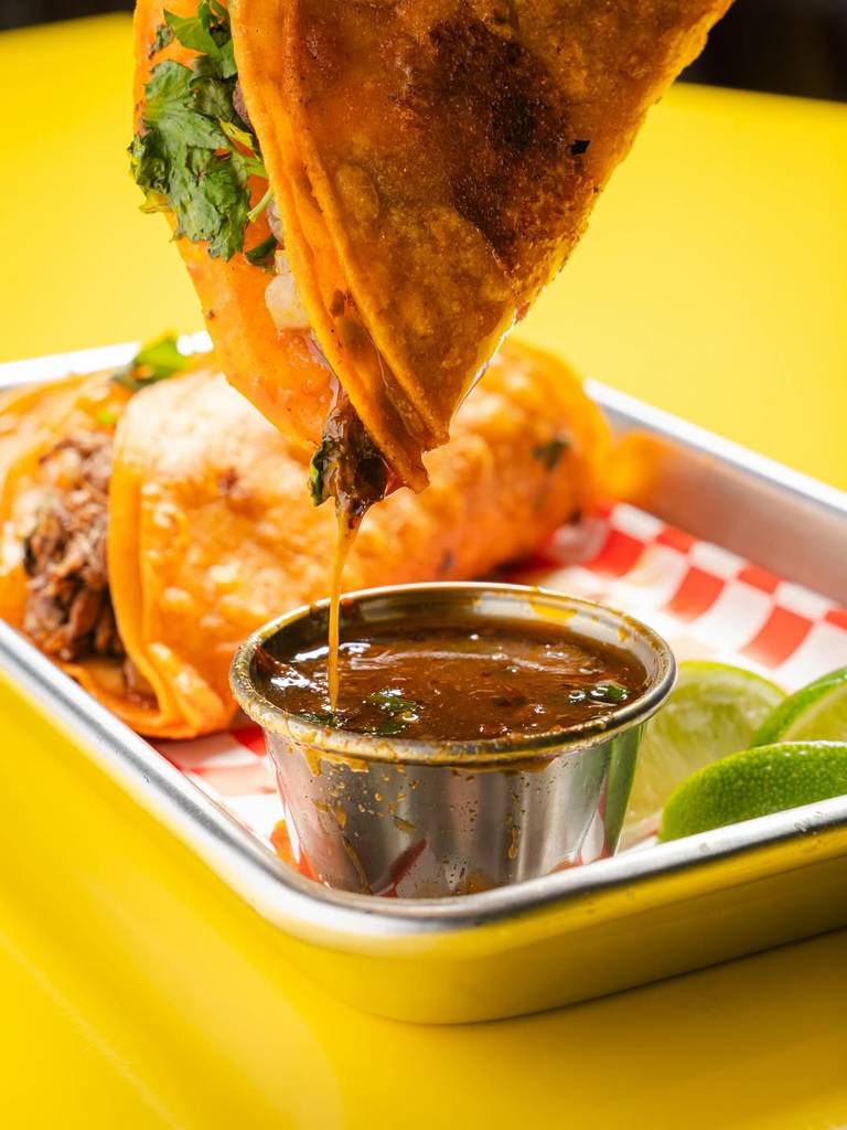 Image shows a taco being dipped into a sauce as featured at Huncho's Tacos in Houston. 