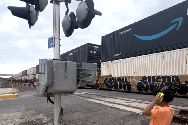 A photo of a child with headphones next to a railroad track in Rosenberg