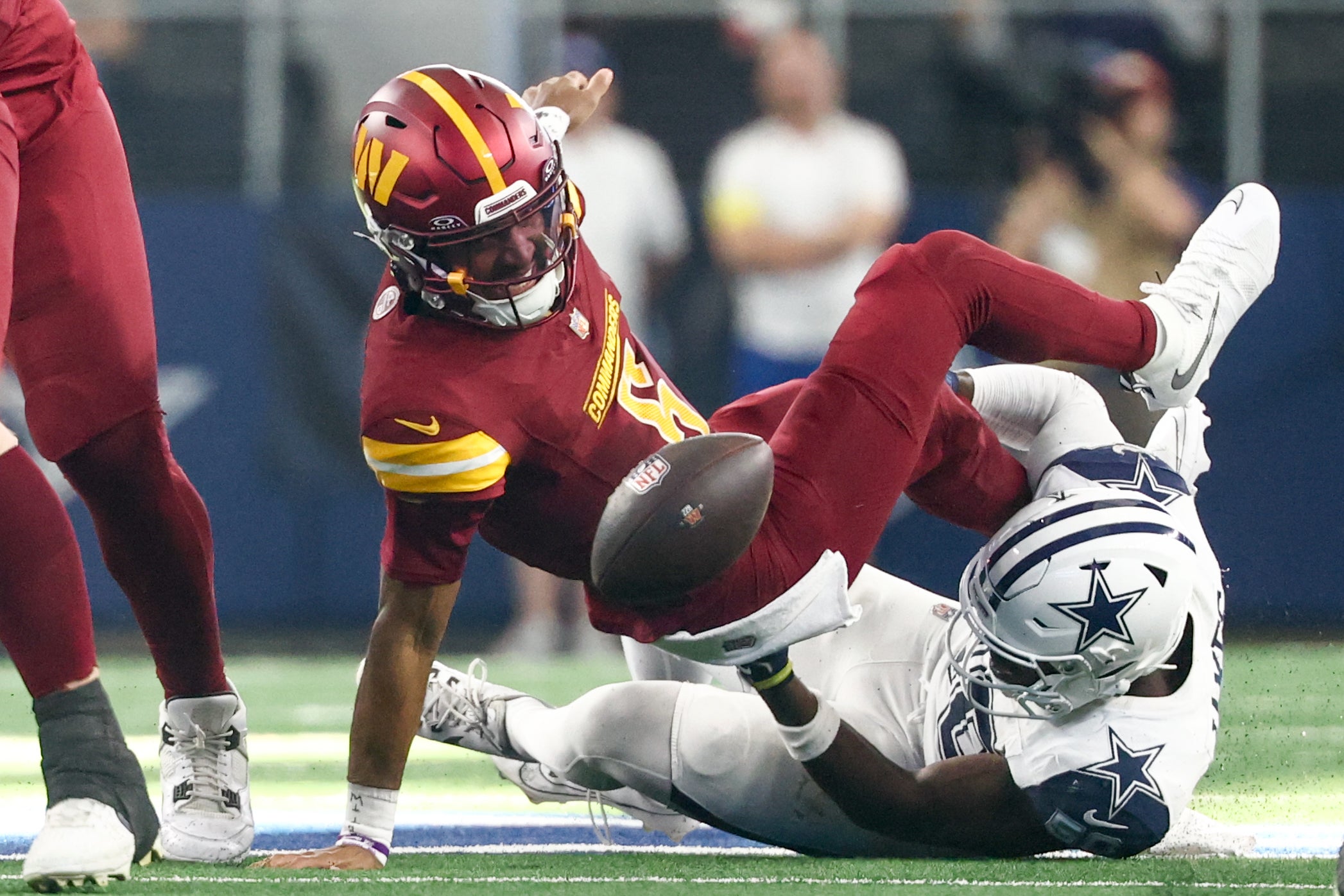 Oct 19, 2025; Arlington, Texas, USA; Washington Commanders quarterback Jayden Daniels (5) fumbles the ball defended by Dallas Cowboys linebacker Shemar James (50) during the third quarter of the game at AT&T Stadium.