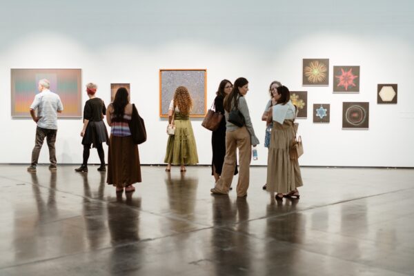 People viewing artworks on a long white wall in an art fair atmosphere.