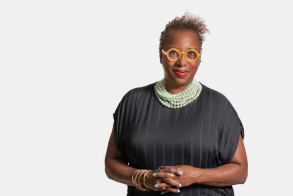 A portrait of curator and museum director Valerie Cassel Oliver, smiling with orange glasses and bead necklace.