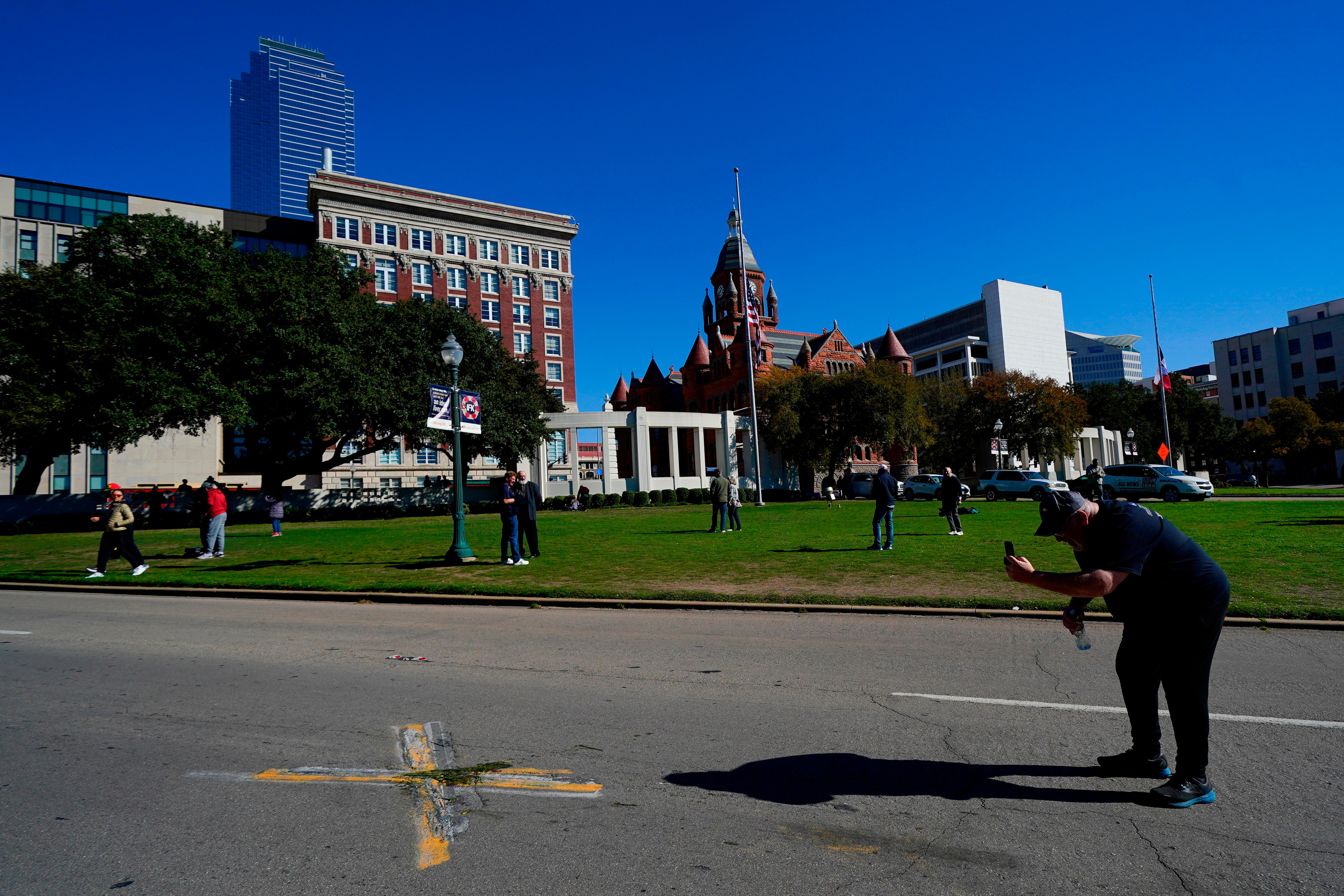 A person uses a cell phone to take pictures of an X on Elm Street at Dealey Plaza