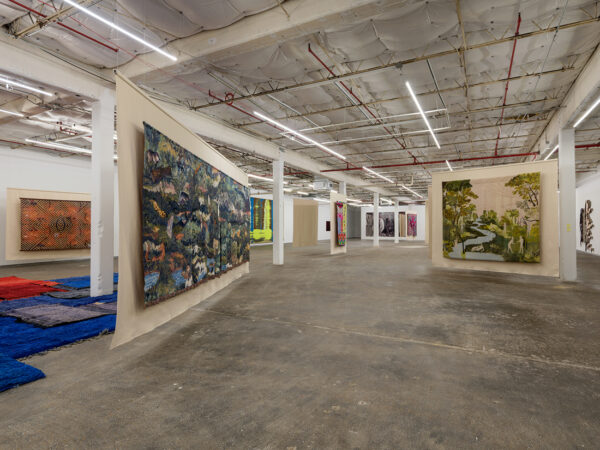 An installation image of various contemporary tapestry artworks hanging in a gallery.