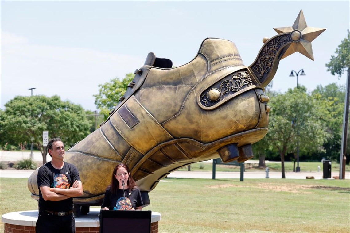 Co-Founders of Street Art for Mankind speaking at podium in front of Texan Golden Boot Sculpture in Arlington on May 28, 2026.