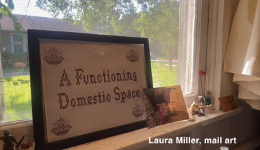 A framed cross-stitch piece reading “A Functioning Domestic Space” sitting on a windowsill.