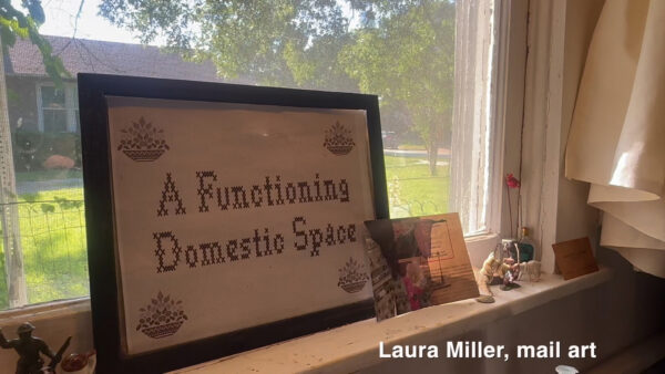A framed cross-stitch piece reading “A Functioning Domestic Space” sitting on a windowsill.