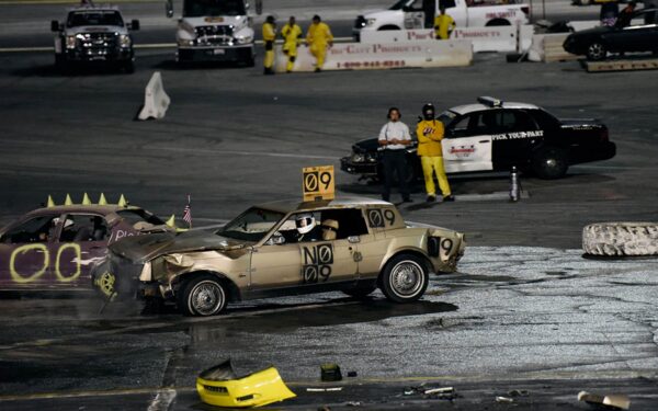 An image of a demolition derby with several standing figures on a racetrack.