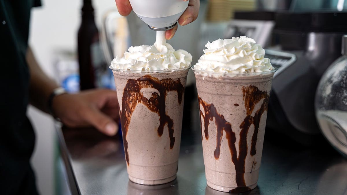 Barista topping two chocolate milkshakes with whipped cream