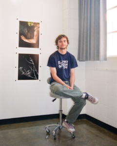image of a man sitting on a stool in front of two images hung up on the wall behind him